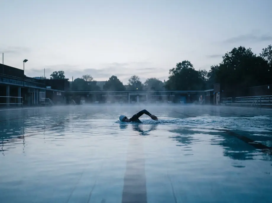A man swimming laps in an outdoor pool at dawn